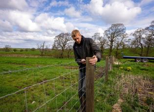 close up of a man fixing a wire fence in a farmers field